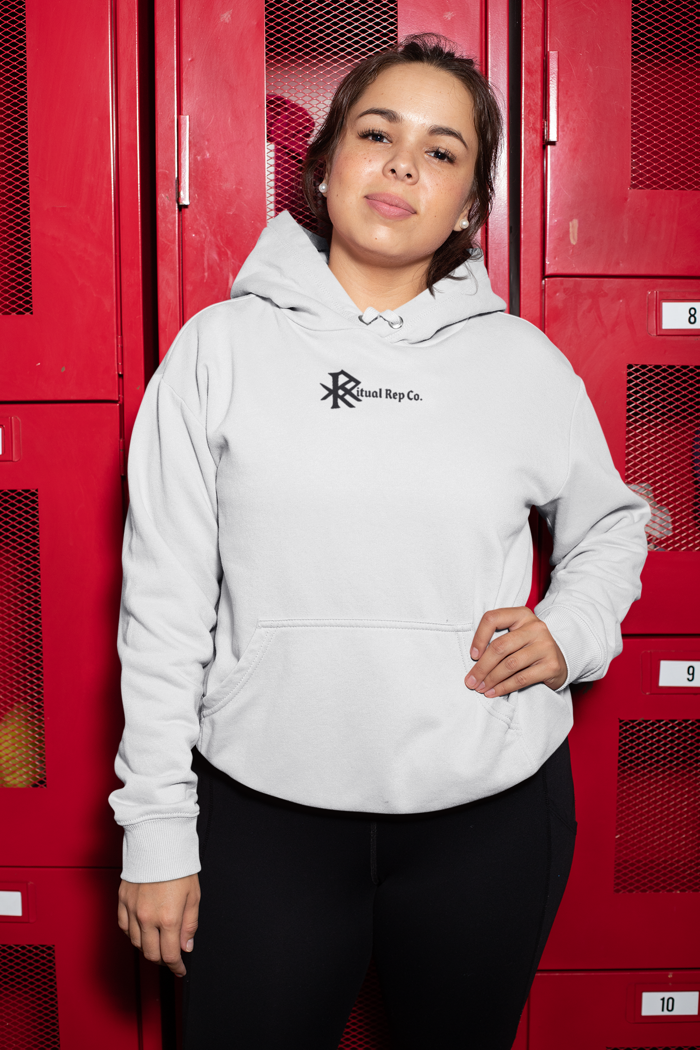 Model in white Initiate Hoodie standing confidently in front of red lockers, front emblem displayed.