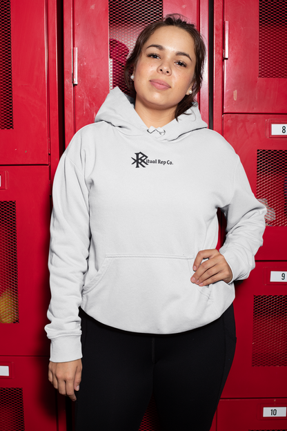 Model in white Initiate Hoodie standing confidently in front of red lockers, front emblem displayed.